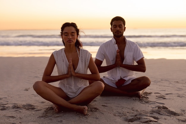 Paar dat yoga samen op het strand uitvoert