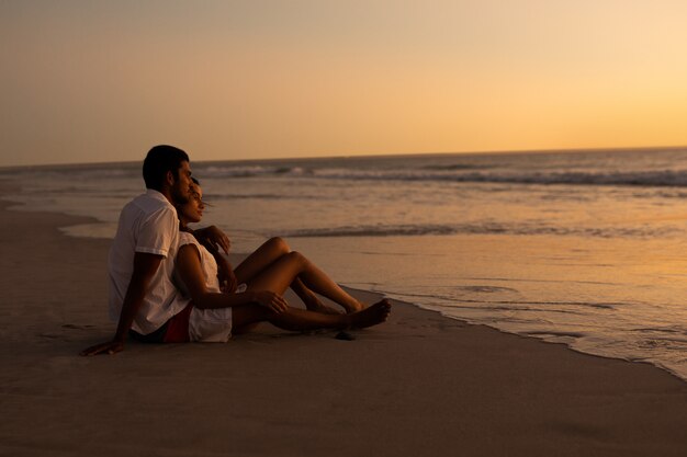 Paar die op zee op het strand tijdens zonsondergang kijken