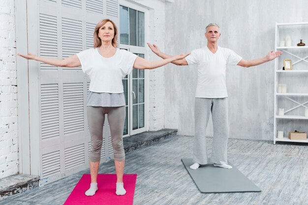 Paar die yoga uitvoeren door wapens outstretching die zich op yogamat bevinden