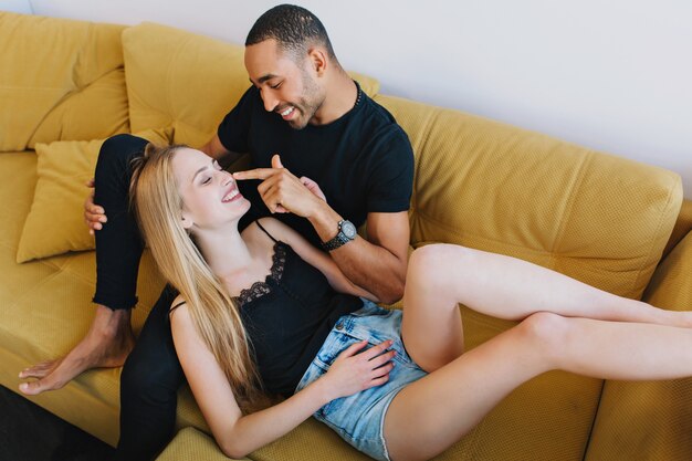 Paar flirten op de bank, plezier maken, glimlachen, tijd samen doorbrengen, ontspannen. Man neus blond aan te raken. Positieve stemming, grappen maken, romantiek, liefde op de knieën