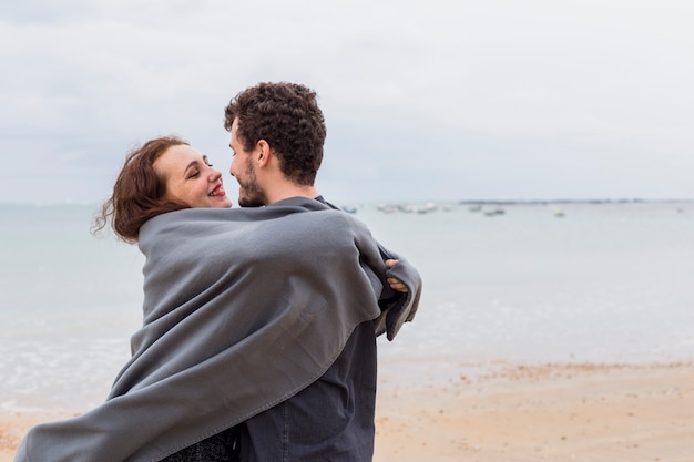 Gratis foto paar in grijze deken knuffelen op zee kust