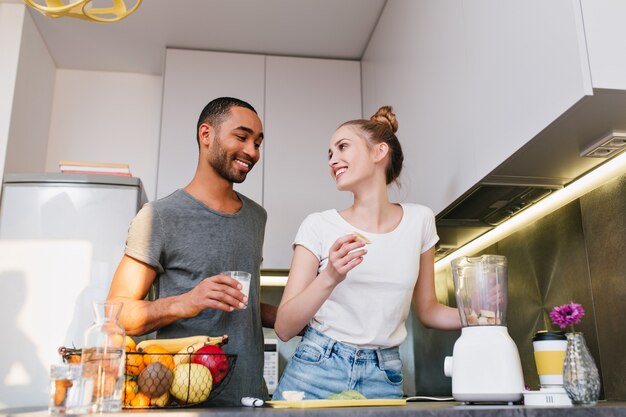 Paar in huiskleren in keuken die met gelukkige gezichten spreken. Paar hebben een praatje en koken tegelijkertijd een maaltijd. Warme relatie, gezond eten, glimlach op gezichten.