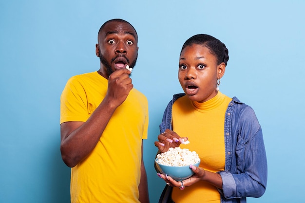 Paar kijken naar enge film op tv en eten popcorn, zijn bang en doodsbang om thrillerfilm in de studio te kijken. Bange vriend en vriendin hebben een snack en kijken naar televisie.