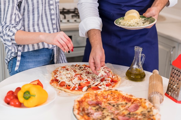 Gratis foto paar kokende pizza met kaas aan tafel