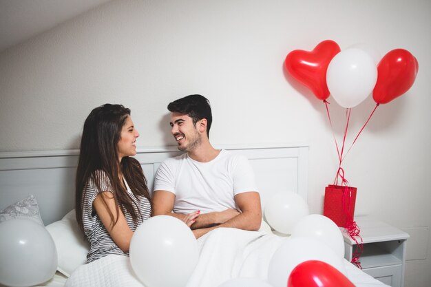 Paar lachen liggend op het bed met ballonnen om hen heen