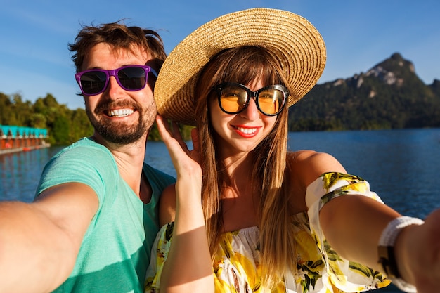 paar markering selfie in de buurt van geweldig uitzicht op het meer en de bergen, stijlvolle kleding en accessoires dragen. Speelse vrolijke sfeer.
