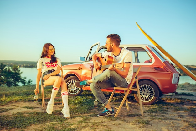 Paar zitten en rusten op het strand gitaar spelen op een zomerdag in de buurt van de rivier