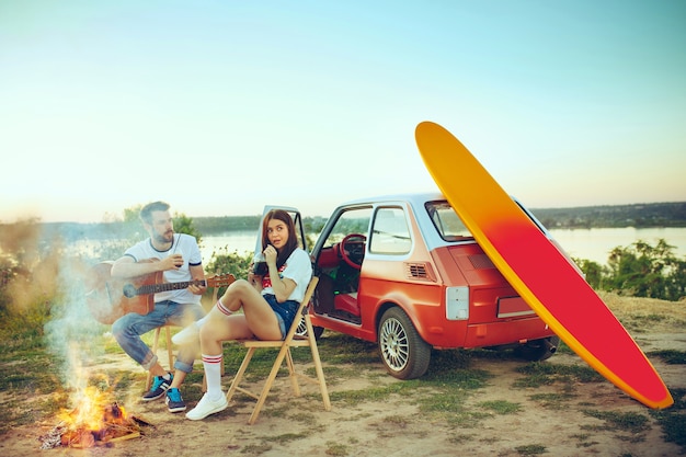 Paar zitten en rusten op strand gitaar spelen op een zomerdag in de buurt van de rivier