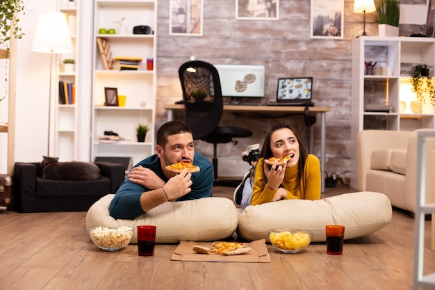 Paar zittend op de vloer en tv kijken in hun woonkamer.