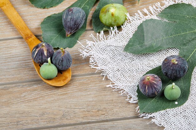 Paarse en groene vijgen op houten tafel met een wit tafelkleed en een blad, een houten lepel.