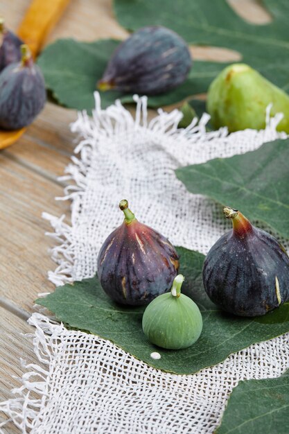 Paarse en groene vijgen op houten tafel met een wit tafelkleed en een blad, een houten lepel.