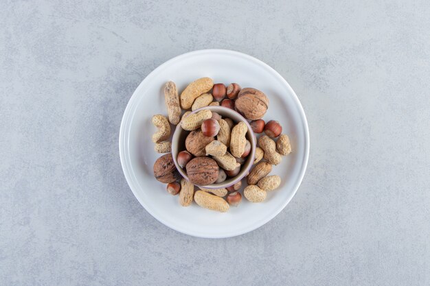 Paarse kom vol met verschillende gepelde noten op stenen achtergrond.