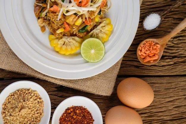 Pad thai in een witte plaat met citroen, eieren en kruiden op een houten tafel.