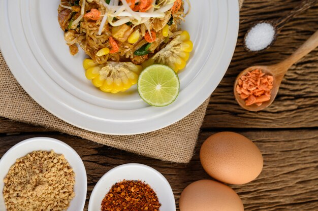 Pad Thai in een witte plaat met citroen, eieren en kruiden op een houten tafel.