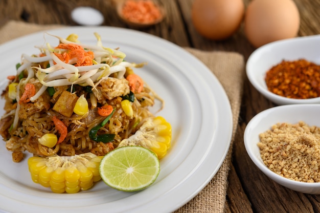 Pad Thai in een witte plaat met citroen, eieren en kruiden op een houten tafel.