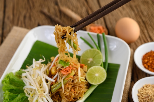 Pad Thai in een witte plaat met citroen, eieren en kruiden op een houten tafel.