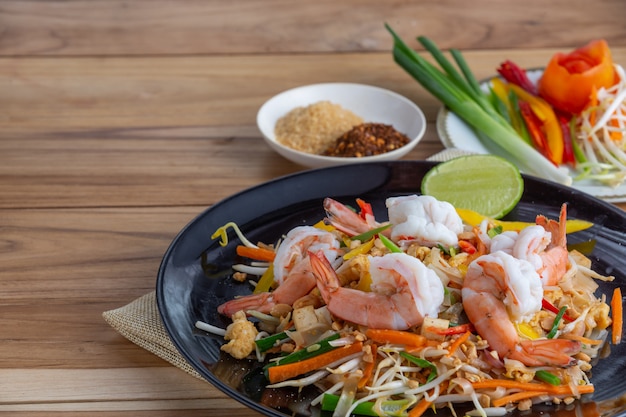 Pad Thai, verse garnalen in een zwarte schotel, geplaatst op een houten tafel.