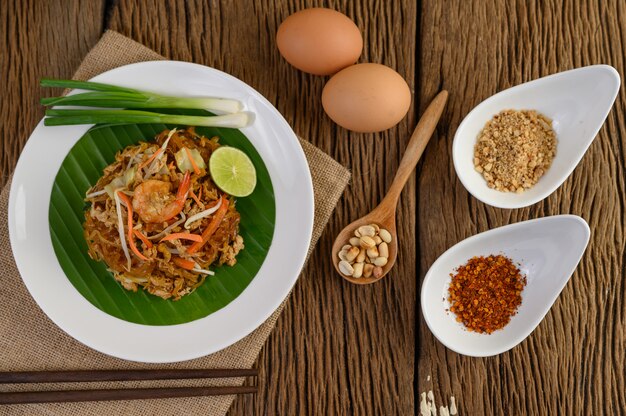 Padthai garnalen in een witte schotel met limoen en eieren op houten tafel.