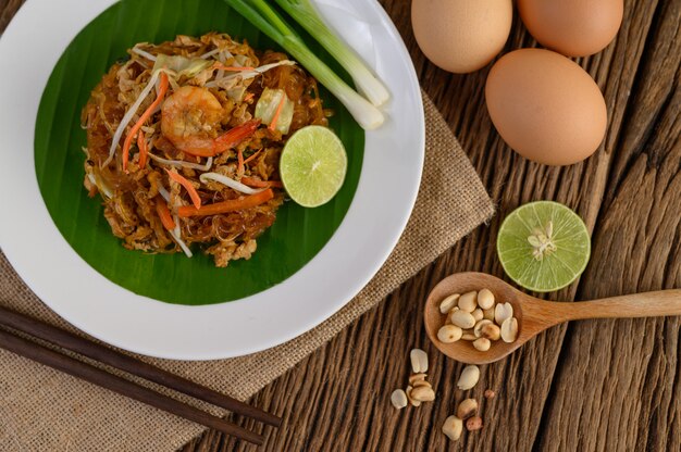 Padthai garnalen in een witte schotel met limoen en eieren op houten tafel.