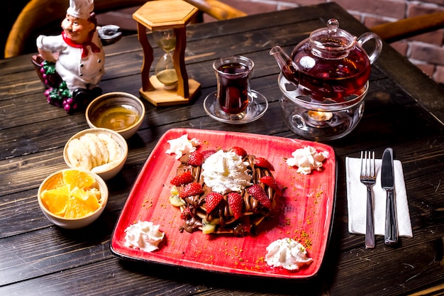 Pannenkoek crème aardbei chocolade saus vruchten en theepot zijaanzicht