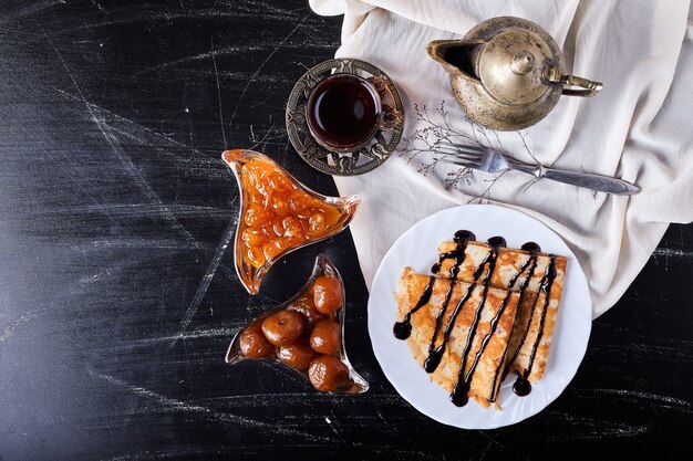 Pannenkoeken in een witte plaat met chocoladesiroop en thee.