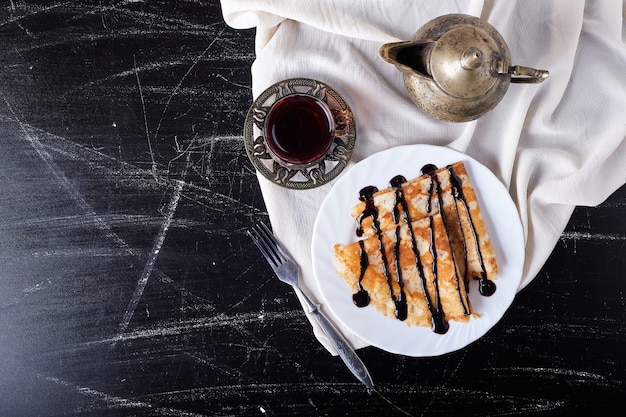 Pannenkoeken in een witte plaat met chocoladesiroop en thee.