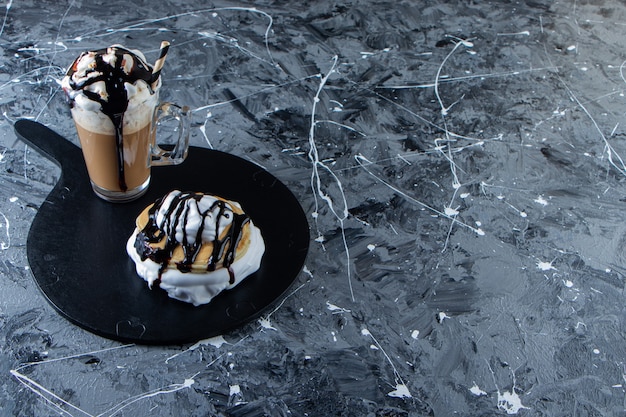 Gratis foto pannenkoeken met chocolade topping en glas koffie op een houten bord.