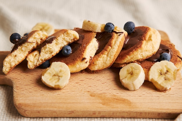 Pannenkoeken met chocoladesaus, bessen en banaan op een houten plaat achter op wit