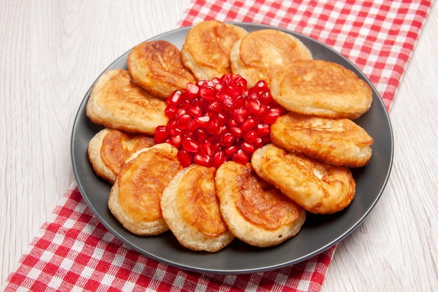 Gratis foto pannenkoekenbord van zijaanzicht met smakelijke pannenkoeken en granaatappel op het geruite tafelkleed op tafel