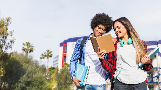 Gratis foto panorama van divers tienerpaar die het boek buiten de campus lezen