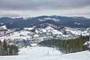 Gratis foto panorama van skigebied, helling, mensen op de skilift, skiërs op de piste tussen groene pijnbomen en sneeuwlansen. ruimte kopiëren