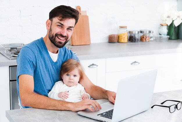 Papa die terwijl het werken aan laptop met baby glimlacht