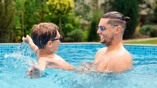Gratis foto papa zwemt met zijn gelukkige zoon in het zwembad