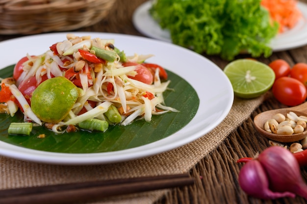 Papajasalade (Som tum Thai) op een witte plaat op een houten lijst.