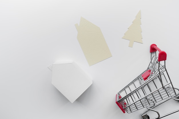 Gratis foto papier uitgesneden huis en kerstboom met miniatuur huis model en winkelwagentje geïsoleerd op een witte achtergrond