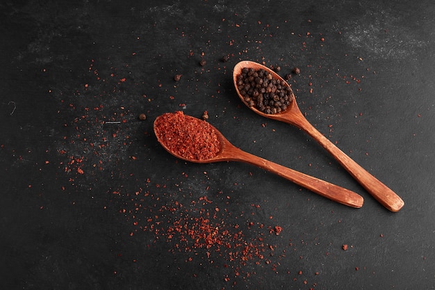 Paprika en zwarte peper in houten lepels.