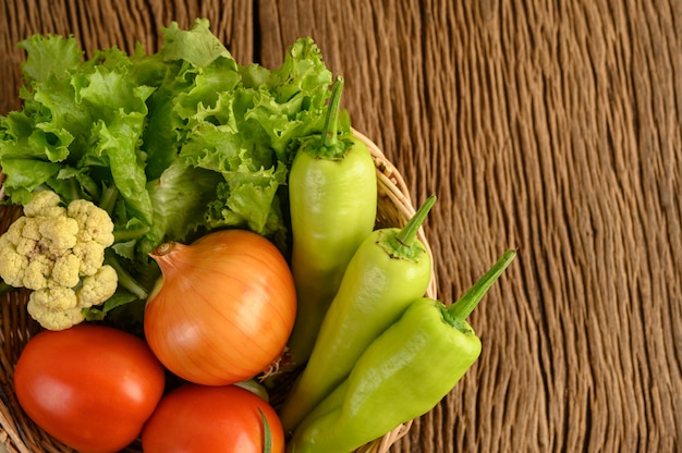 Paprika, tomaat, ui, salade en bloemkool op een houten mand en houten tafel.