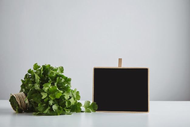 Partij verse groene peterselie koriander gebonden met ambachtelijke touw in de buurt van krijtbord prijskaartje geïsoleerd op een witte tafel