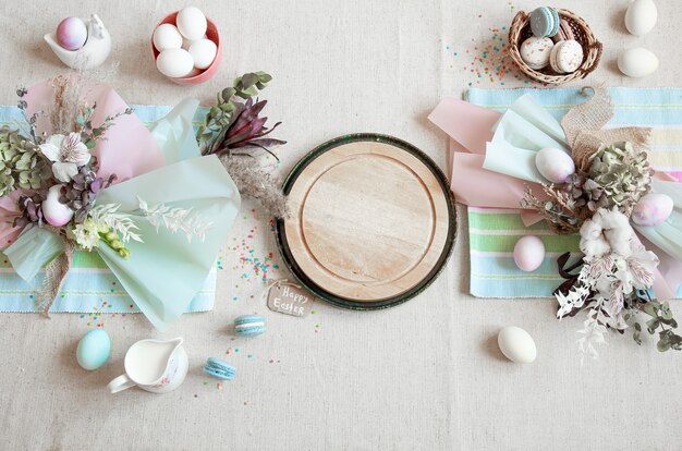 Pasen-samenstelling met bloemen, eieren en houten ruimte voor tekst in vlakke pastelkleuren.