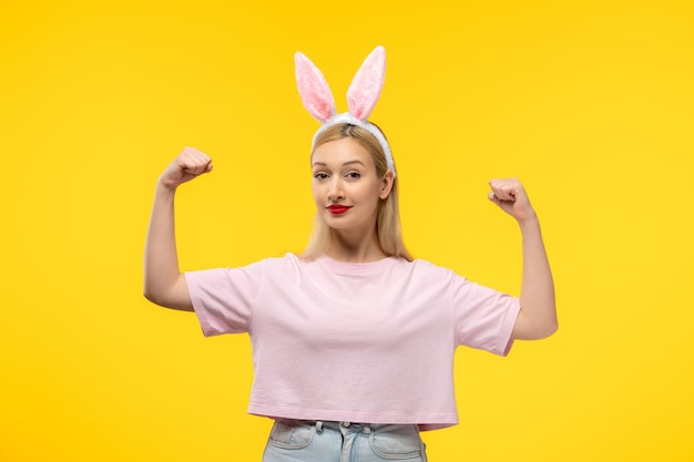 Pasen schattig jong blond meisje met roze konijnenoren die biceps laten zien