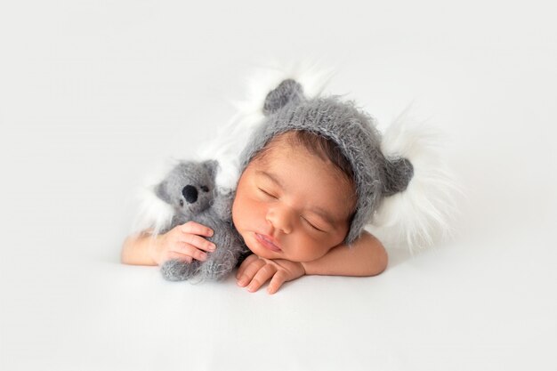 Pasgeboren rusten in kleine schattige grijze hoed en met grijze speelgoed beer in zijn handen