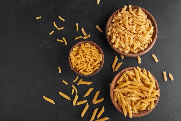 Pasta in houten bekers op zwarte achtergrond, bovenaanzicht.