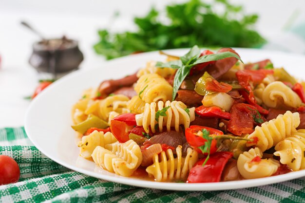 Pasta met tomatensaus met worst, tomaten, groene basilicum ingericht in witte plaat op een houten tafel.