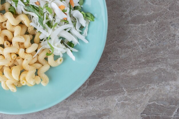 Pasta met verse salade en ei op blauw bord.