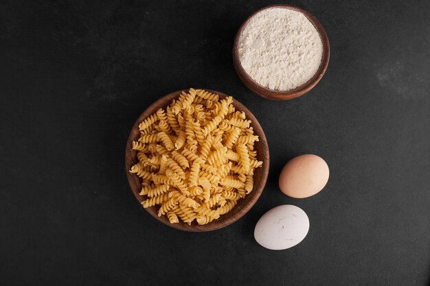 Pasta's in een houten beker met ingrediënten eromheen.