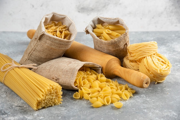 Pastasoorten in rustieke mand met een houten rollend roze op marmeren tafel.