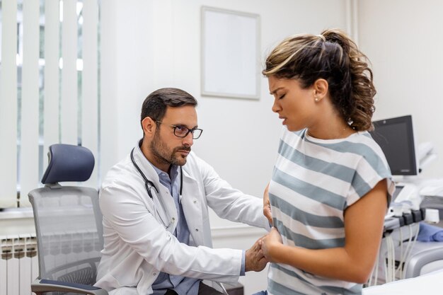 Patiënt vertelt arts over haar pijn en gezondheidsproblemen tijdens bezoek aan ziekenhuis Jonge vrouw klaagt over rug- of nierpijn terwijl ze op onderzoeksbed zit bij de dokter