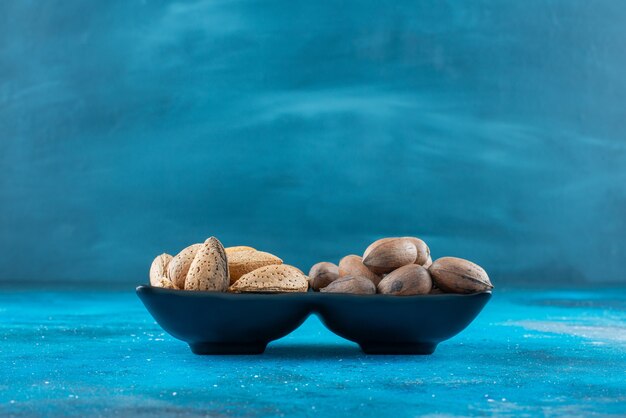 Pecannoten en amandelen in een kom, op de blauwe tafel.