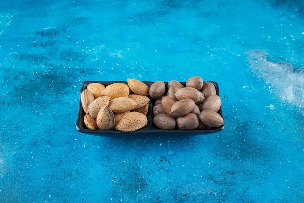 Pecannoten en amandelen in een kom, op de blauwe tafel.
