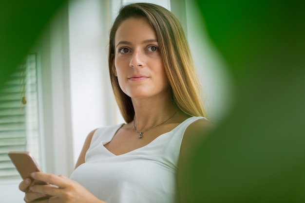 Peinzende aantrekkelijke jonge vrouw met behulp van mobiele telefoon